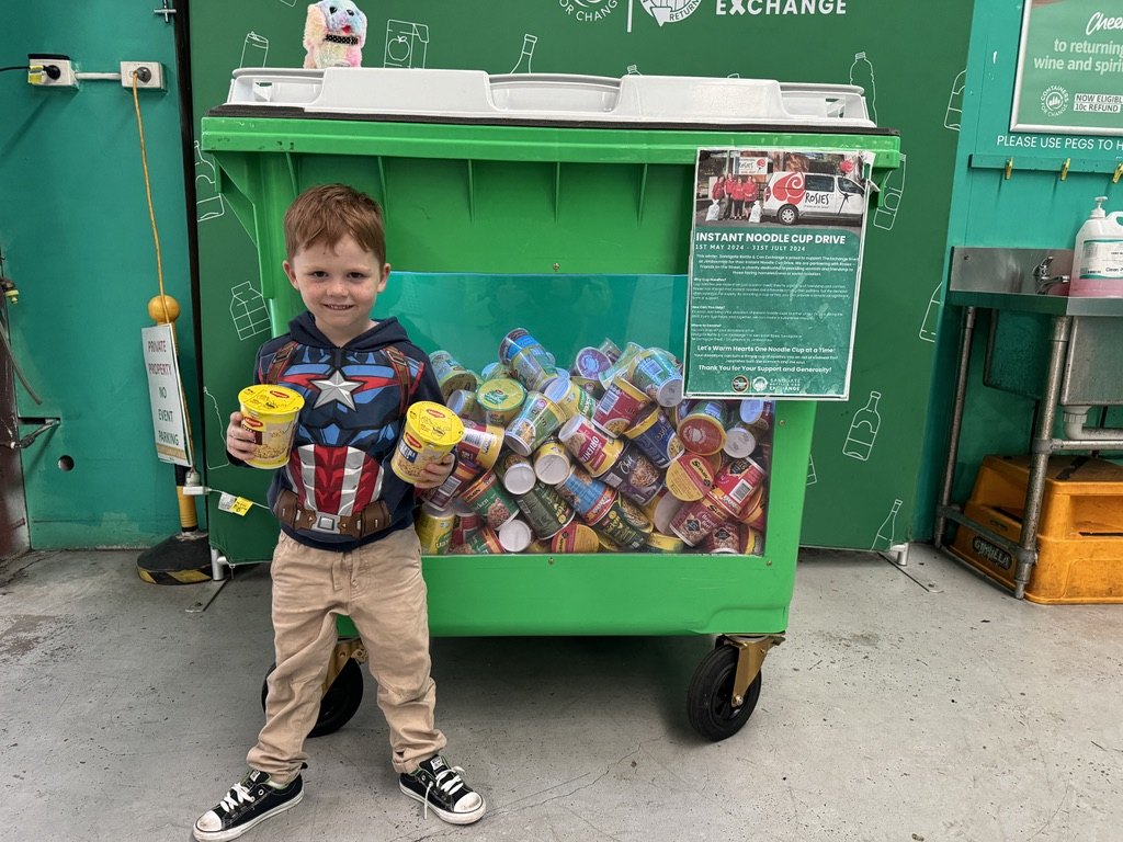 A young local supporter standing beside a Sandgate Bottle & Can Exchange community collection bin.