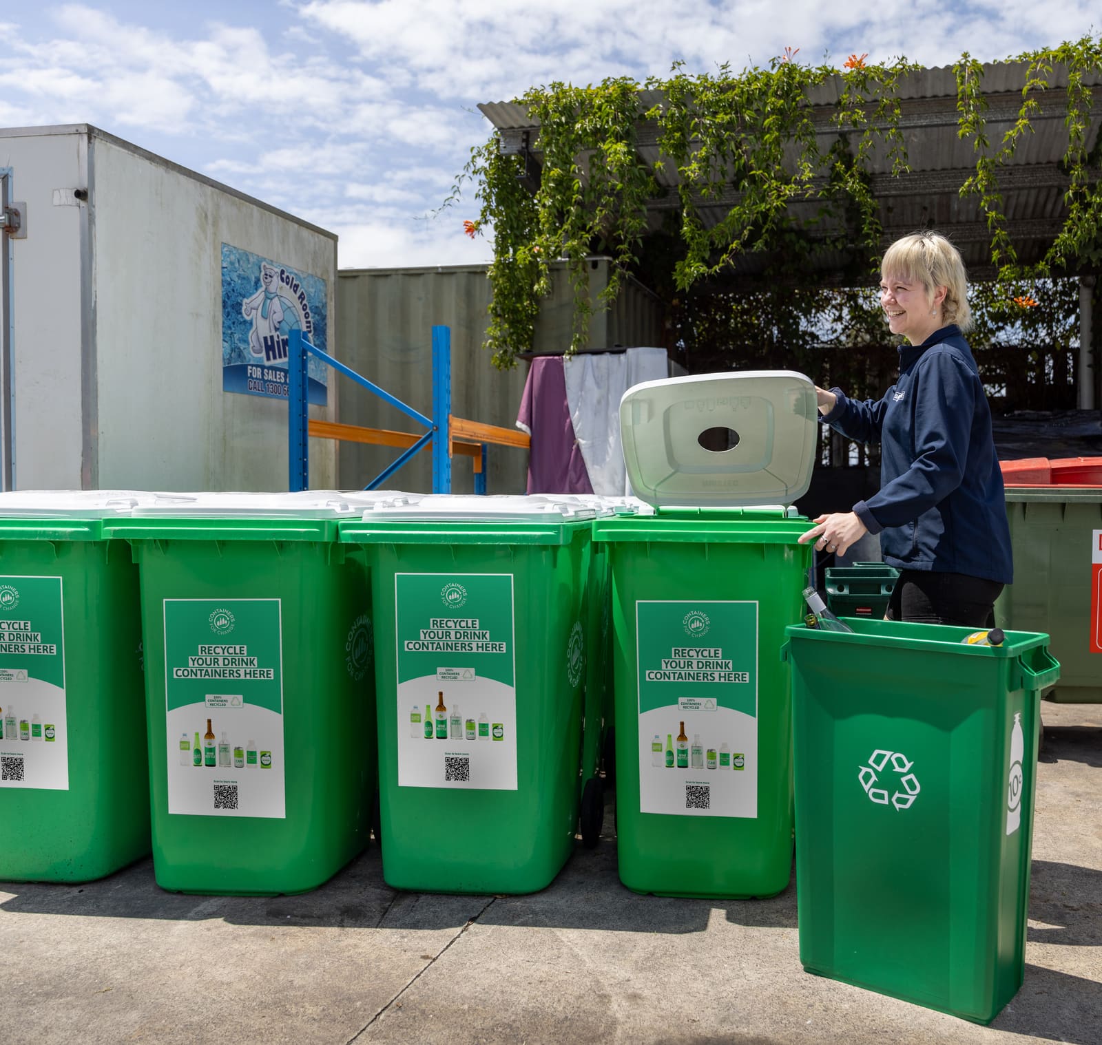 A collection team member with a row of green commercial drink-container bins.