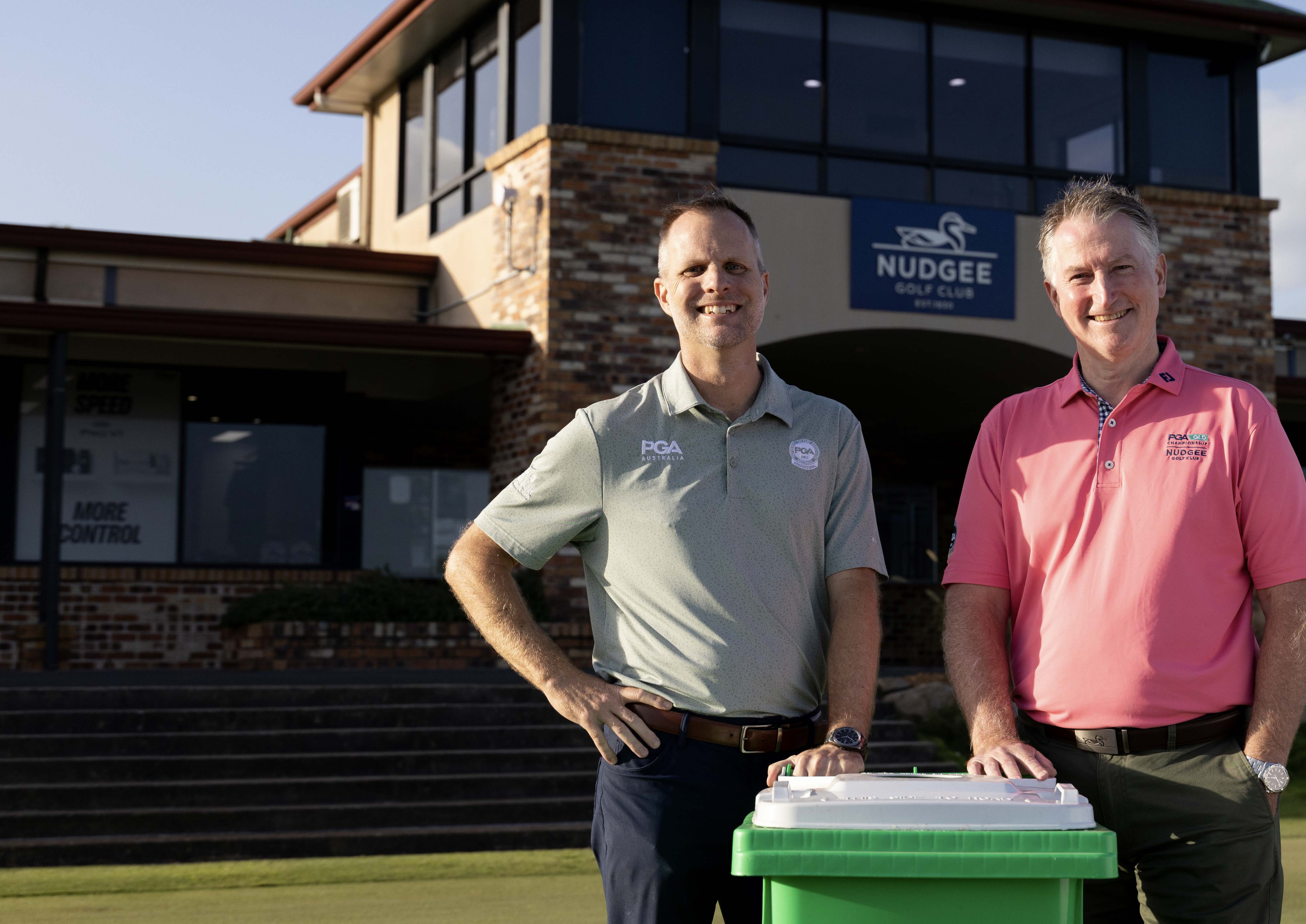 Two Nudgee Golf Club team members standing with a green Containers for Change bin outside the clubhouse.