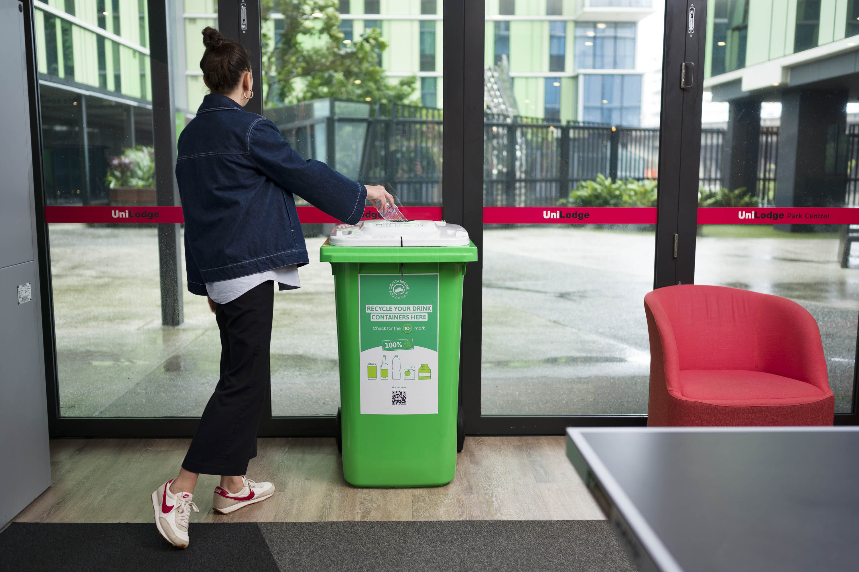 A resident placing an eligible drink container into a green Containers for Change bin.